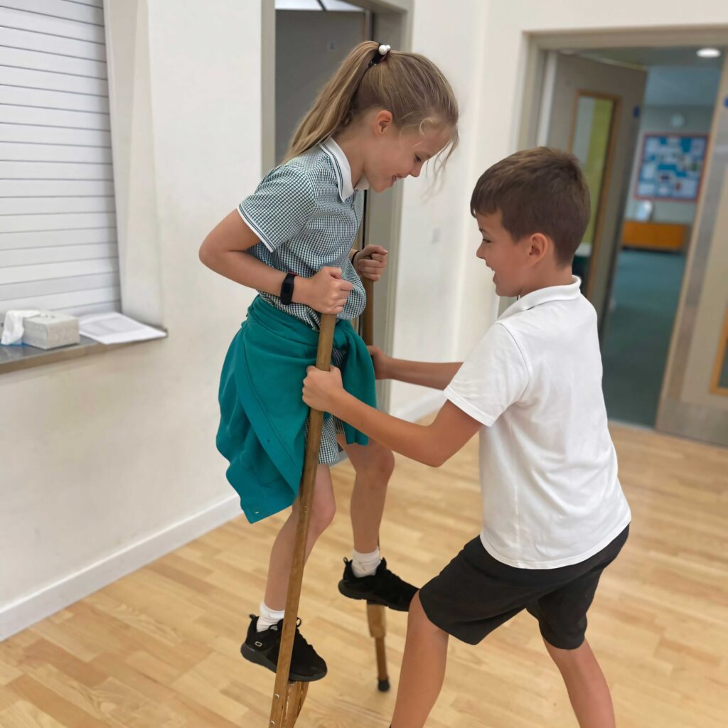 stilt-assisst button 1024 2 school children practice stilt walking together.